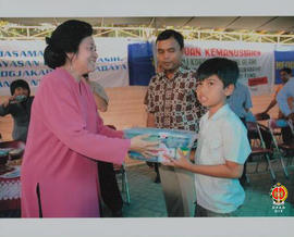 Seorang anak sedang menerima bantuan satu kotak makanan kecil yang diserahkan langsung oleh pimpi...